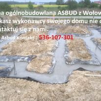 Fundamenty domu w trakcie wylewania betonu, widoczna folia izolacyjna i zbrojenie, w tle pole uprawne i reklama firmy budowlanej.