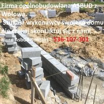 Wznoszenie fundamentów z bloczków betonowych, widoczne zbrojenie, ziemia i informacja kontaktowa firmy budowlanej.