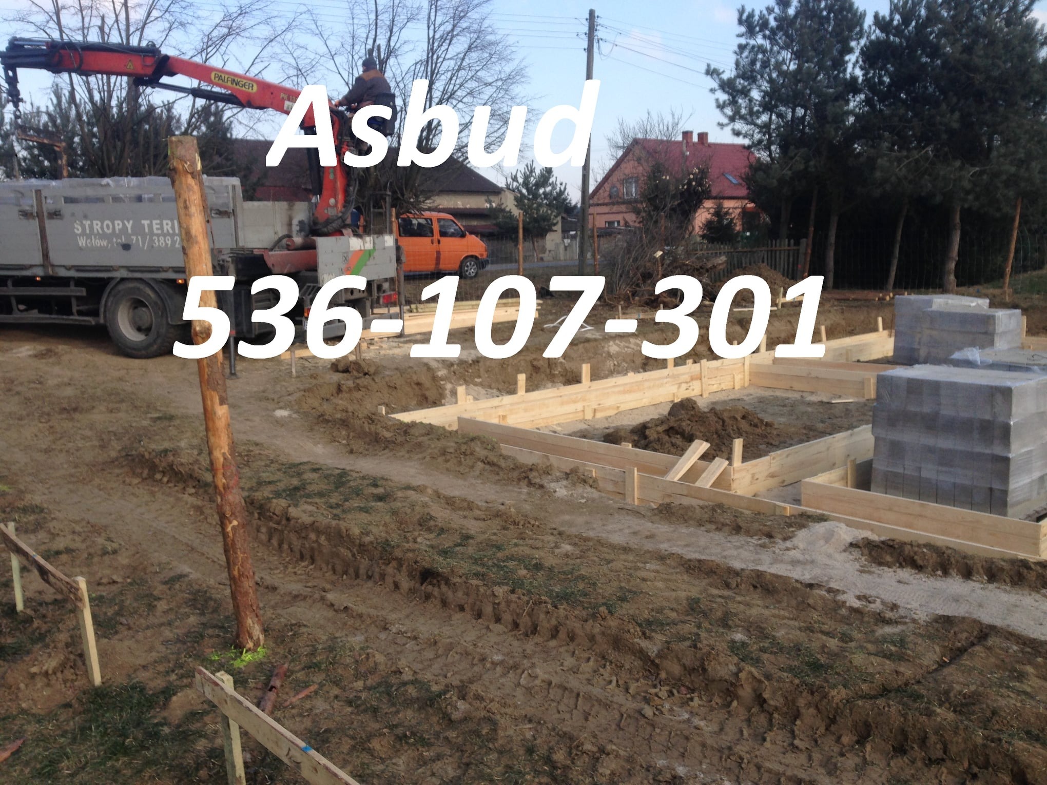 Fundamenty domu w trakcie budowy: szalunki drewniane, palety z bloczkami betonowymi, dźwig Palfinger i pomarańczowy bus w tle.