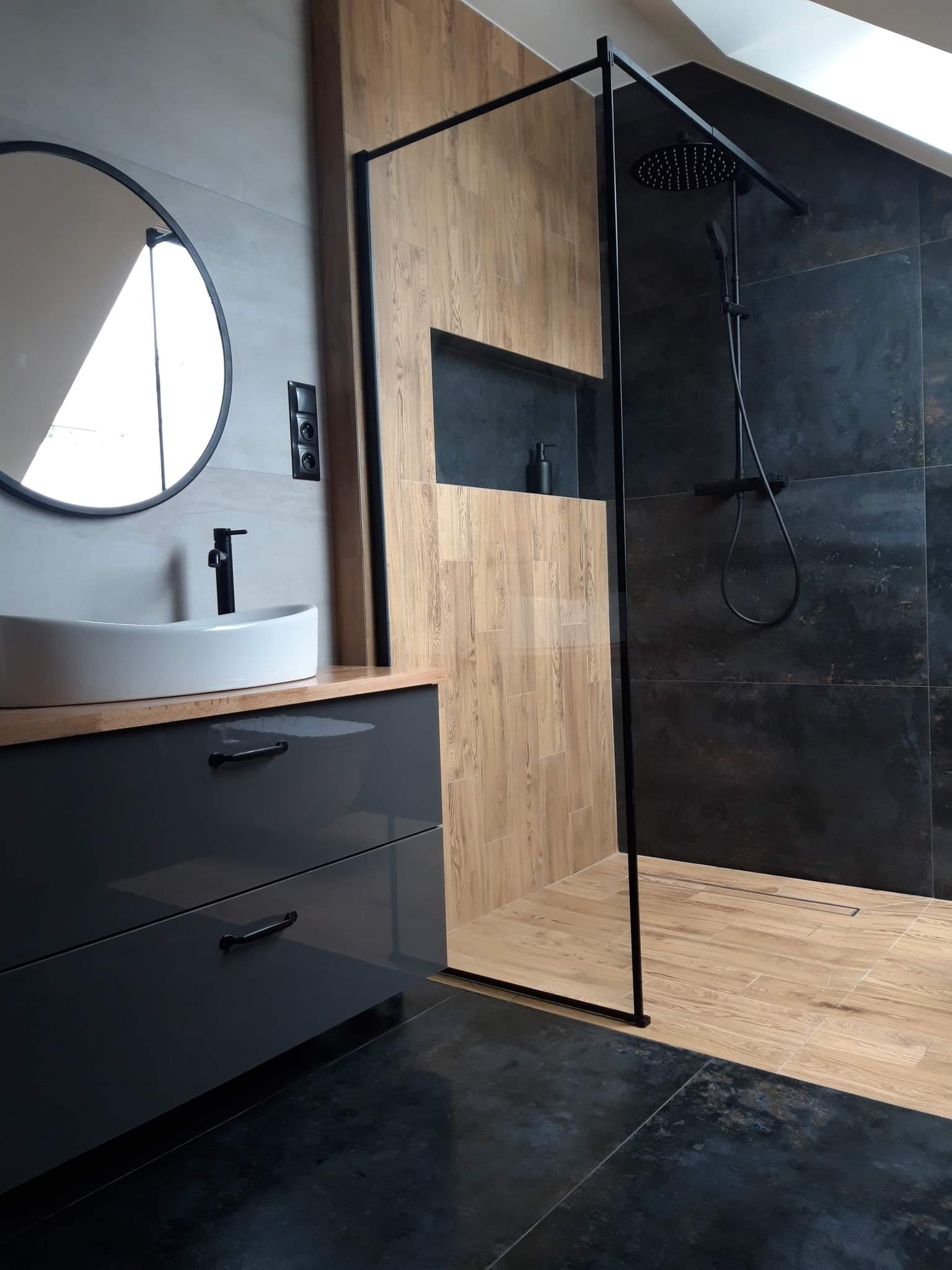 Nowoczesna łazienka z kabiną typu walk-in, czarną armaturą i umywalką nablatową na szafce z szufladami, wykończona płytkami imitującymi drewno i ciemnym gresem.
