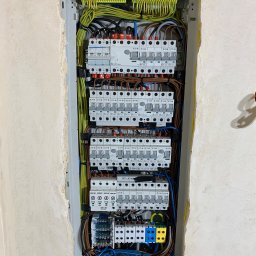 Łukasz polis - Rozdzielnica elektryczna z licznymi bezpiecznikami i przewodami w ścianie, widok z bliska. Elementy marki Eaton i Hager. Ściana w stanie surowym.