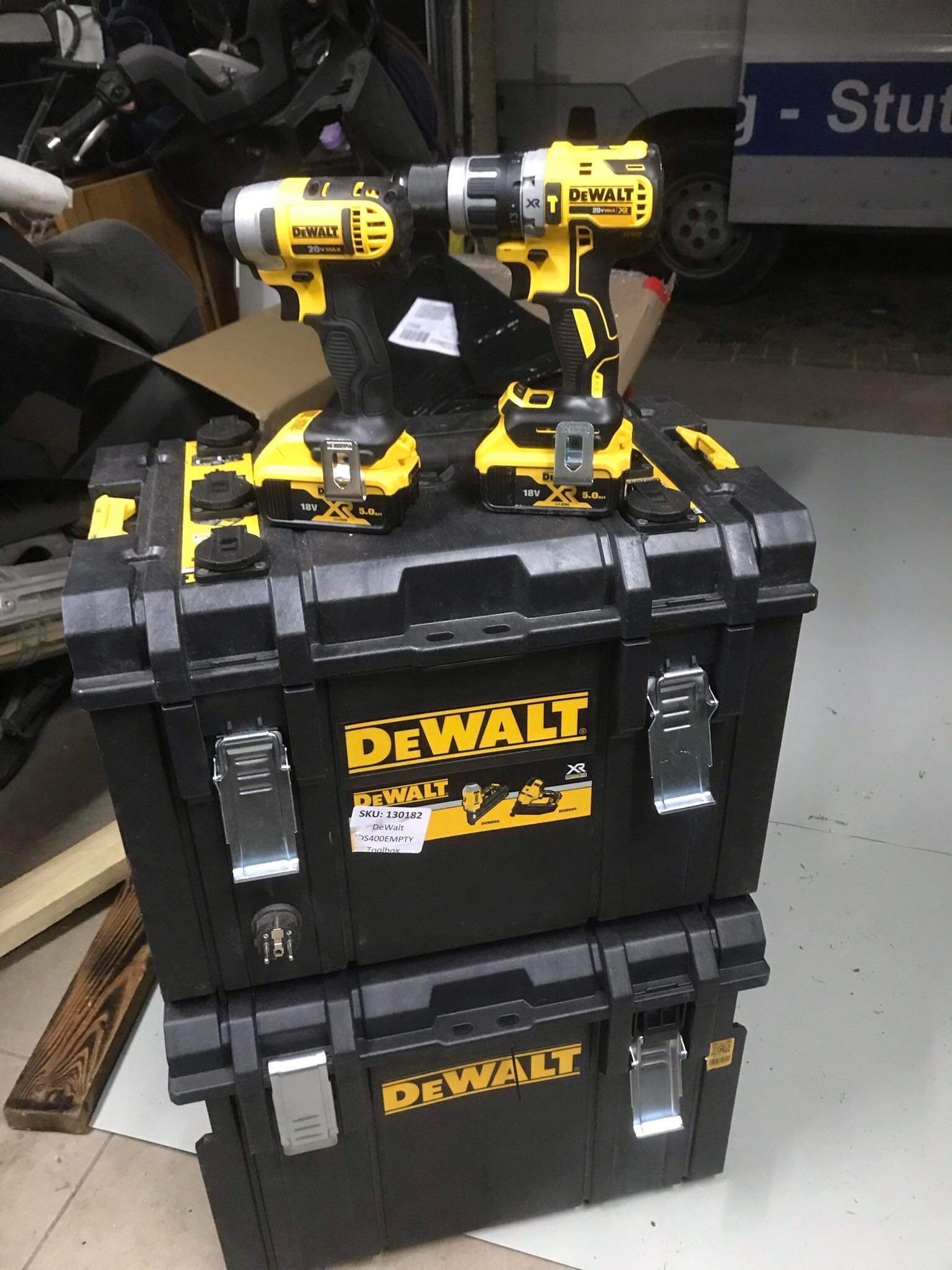 Dwie żółto-czarne wiertarki akumulatorowe DeWalt 20V MAX i 18V XR 5.0Ah stojące na czarnych skrzynkach narzędziowych DeWalt DS400EMPTY Toolbox, z widocznymi etykietami SKU: 130182, w tle części...