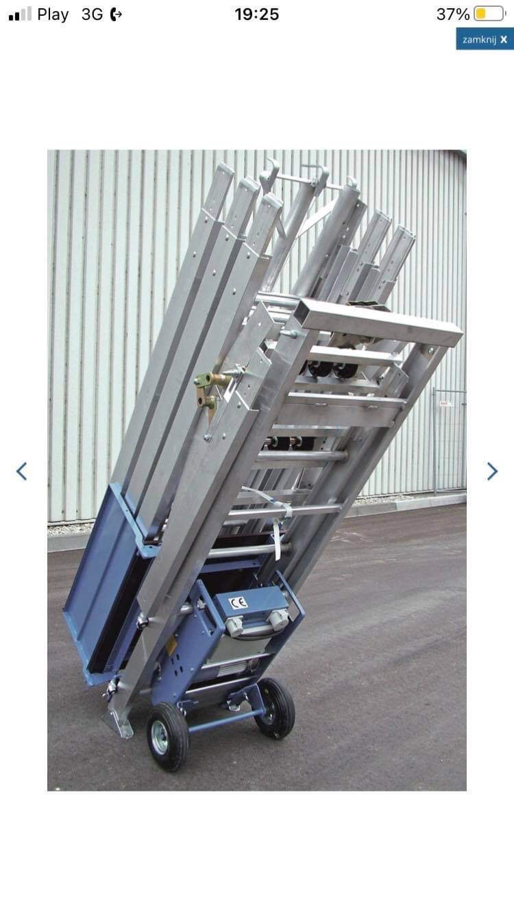 Podnośnik dekarski z platformą, widoczne elementy konstrukcyjne i mechanizm podnoszenia, na tle szarej ściany.