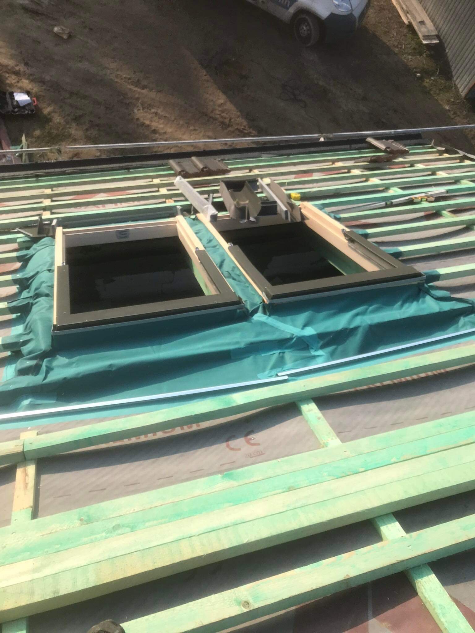 Montaż okien dachowych na nowej konstrukcji dachu z widocznymi łatami i kontrłatami w kolorze zielonym, zabezpieczonych folią hydroizolacyjną.