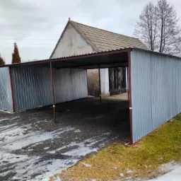 Zadaszone stanowisko parkingowe z blachy falistej na posesji w pochmurny dzień, widoczne pozostałości śniegu na podłożu.