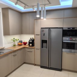 Meble na wymiar - Paweł Piórkowski - Nowoczesna kuchnia na wymiar w odcieniach beżu, z drewnianym blatem i sprzętem AGD w zabudowie. Widoczne oświetlenie punktowe i dekoracje na blacie.