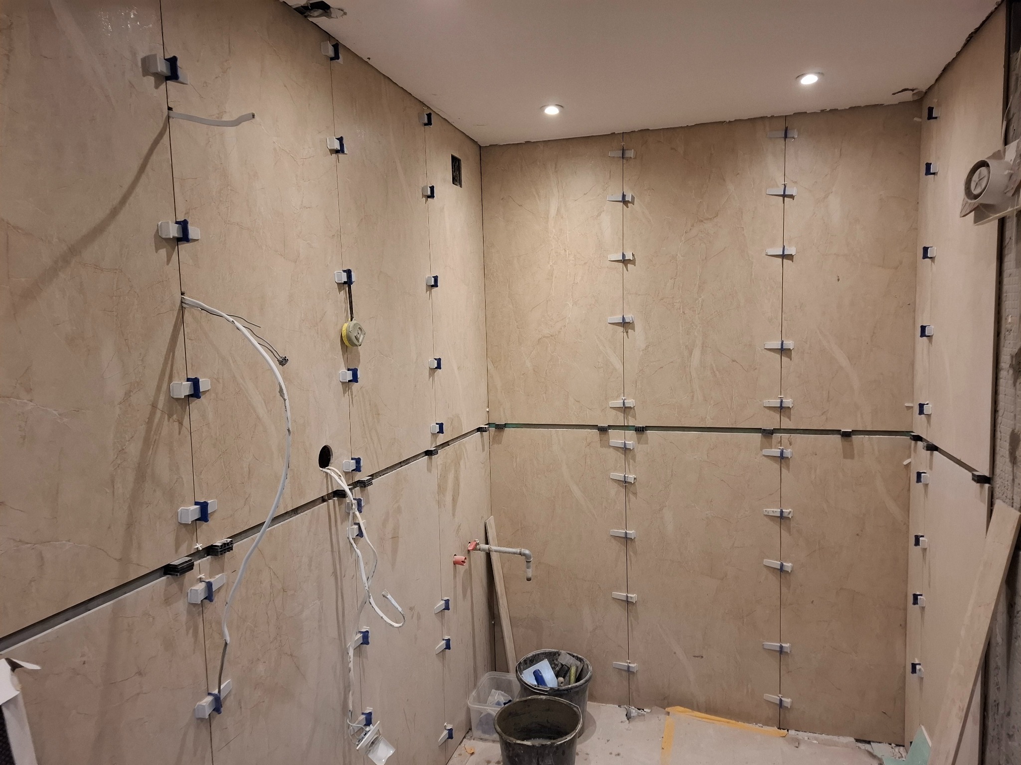 Układanie płytek w Nałęczowie z użyciem systemu poziomowania. Widoczne fragmenty instalacji i narzędzia. Beżowe płytki imitujące marmur, jasne oświetlenie.