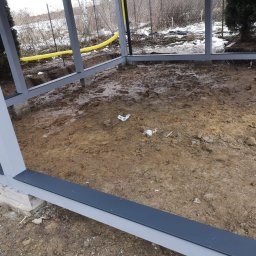 GregBud - Stalowa konstrukcja szkieletowa w trakcie budowy, widoczny fundament i fragment żółtego przewodu w ziemi.