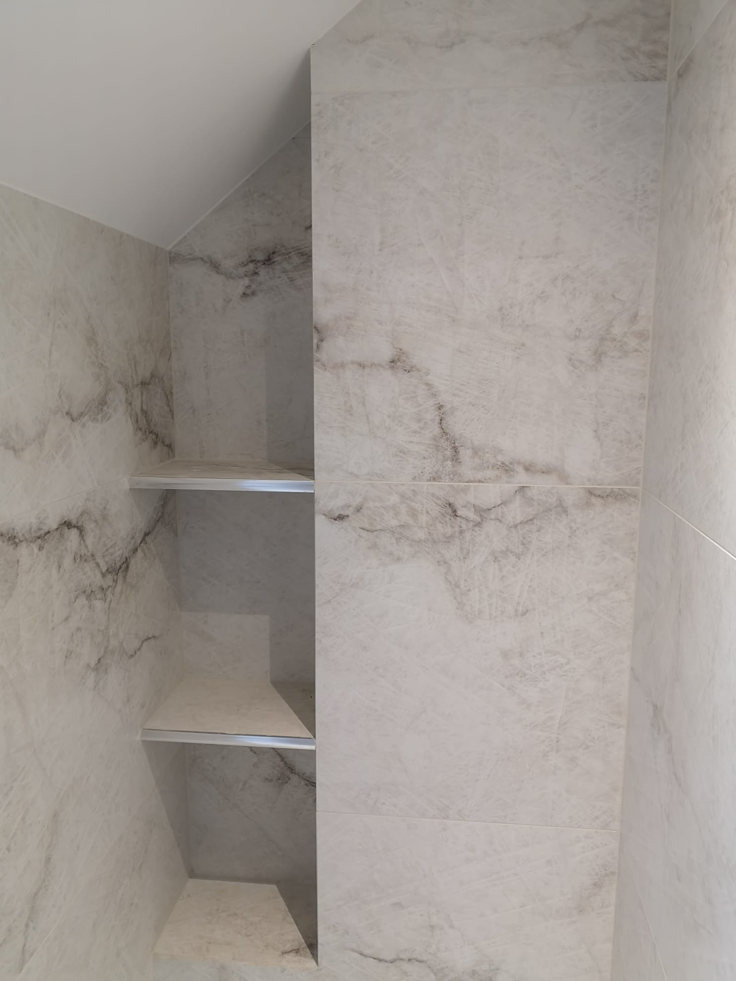 Wnęka z trzema półkami wyłożona płytkami imitującymi marmur w odcieniach bieli i szarości.