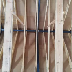 Konstrukcja dachu z drewnianych krokwi wzmocniona stalowymi elementami, widoczne płyty OSB z nadrukiem, perspektywa od wewnątrz.