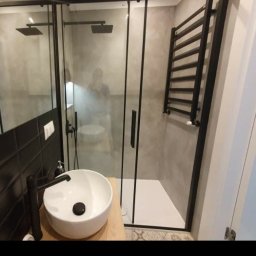 Łukasz Brzeski - Nowoczesna łazienka z kabiną prysznicową typu walk-in z czarnymi ramami, okrągłą umywalką nablatową i grzejnikiem drabinkowym w tym samym kolorze.