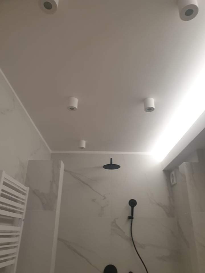 Nowoczesna łazienka z marmurowymi płytkami, czarną armaturą i oświetleniem punktowym LED.