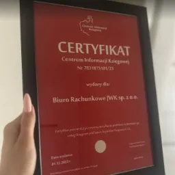 Certyfikat Centrum Informacji Księgowej w czarnej ramce, trzymany w dłoni, wydany dla Biura Rachunkowego JWK sp. z o.o., potwierdzający pozytywną weryfikację usług księgowych.