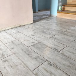 Super Mario Usługi Remontowo-Budowlane - Ułożona podłoga z płytek imitujących drewno, widoczne schody i ściana w trakcie remontu, butelka wody przy schodach.