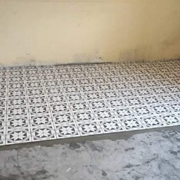 Super Mario Usługi Remontowo-Budowlane - Fragment podłogi z ułożonymi płytkami ceramicznymi o wzorze geometrycznym w odcieniach szarości i bieli, widoczny świeży klej i narzędzia glazurnicze w rogu pomieszczenia.