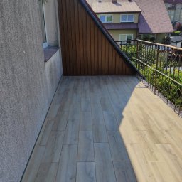 Super Mario Usługi Remontowo-Budowlane - Balkon po remoncie z drewnopodobną podłogą z płytek, brązową boazerią na ścianie szczytowej i ozdobną metalową balustradą.