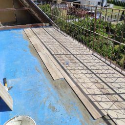Super Mario Usługi Remontowo-Budowlane - Balkon w trakcie układania płytek imitujących drewno na niebieskiej hydroizolacji, widoczne krzyżyki dystansowe i narzędzia, w tle balustrada i zabudowa domów.