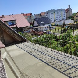 Super Mario Usługi Remontowo-Budowlane - Wylewka betonowa na balkonie z kutą, rdzawą balustradą, widok na zabudowę miejską w słoneczny dzień.
