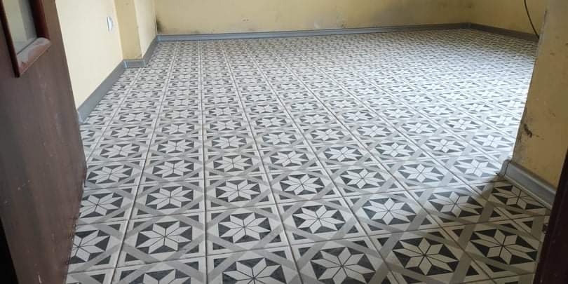 Nowo ułożona podłoga z szarych i białych płytek ceramicznych z geometrycznym wzorem gwiazdy i rombu, widok z perspektywy drzwi.