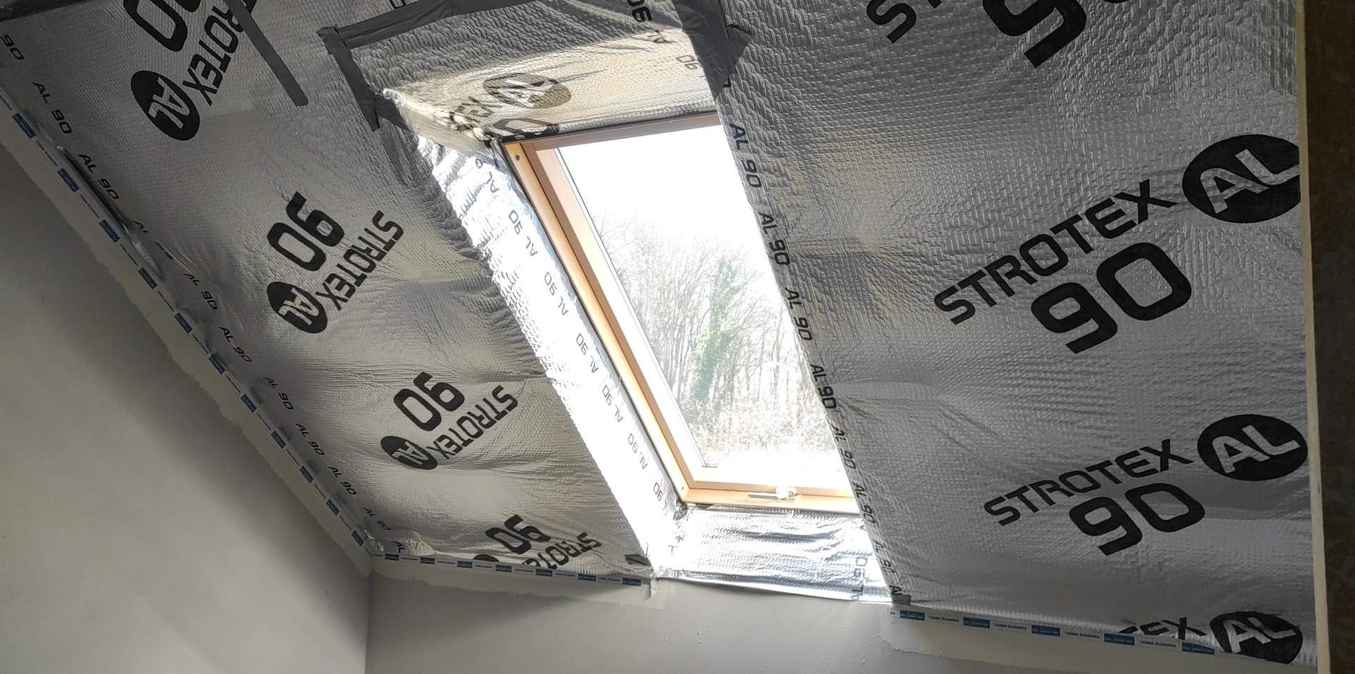 Poddasze z oknem połaciowym w trakcie ocieplania, widoczna folia paroizolacyjna Strotex AL 90, zabezpieczająca konstrukcję przed wilgocią.