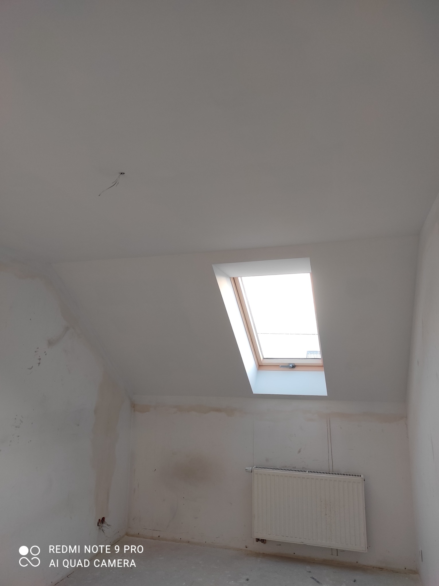 Pokój na poddaszu w trakcie przygotowań do malowania, widoczne ślady po szpachlowaniu na ścianach, grzejnik oraz okno dachowe.