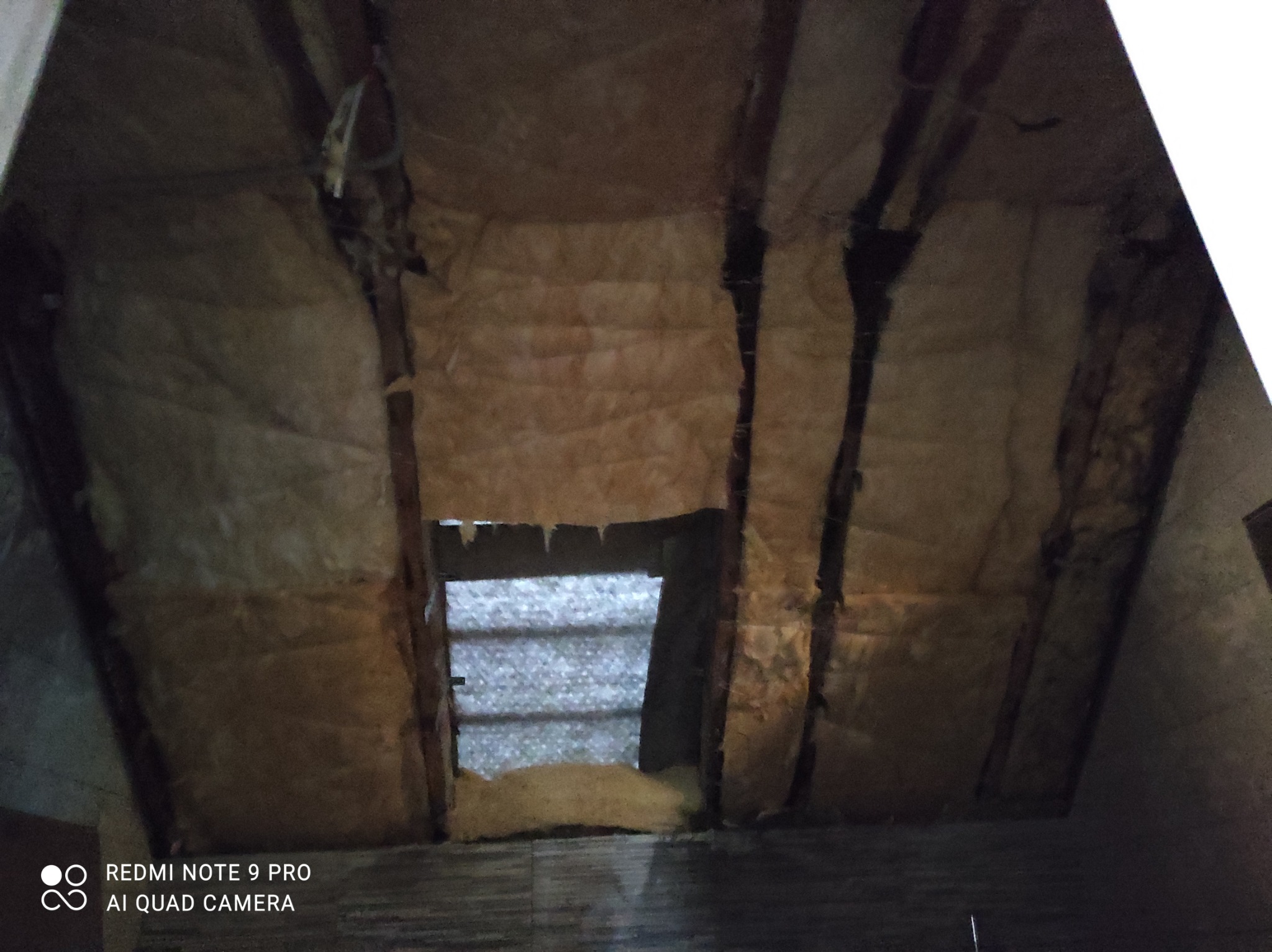 Poddasze w trakcie ocieplania, widoczne drewniane belki konstrukcyjne i warstwa izolacji z wełny mineralnej, z fragmentem okna dachowego