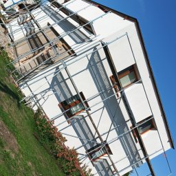 Rafał Iwiński - Dom jednorodzinny w trakcie prac elewacyjnych, widoczne rusztowania i świeżo pomalowana biała fasada, na pierwszym planie ogródek z kamieniami.