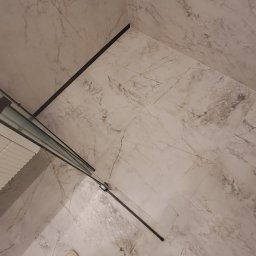 Andrii Kulchenko - Wykończona kabina prysznicowa z marmurowymi płytkami, widok z góry na podłogę i fragment osoby w ubrudzonych farbą spodniach i butach.