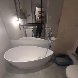 Andrii Kulchenko - Nowoczesna łazienka z wolnostojącą białą wanną, szarą glazurą, toaletą i odbiciem osoby robiącej zdjęcie w lustrze.