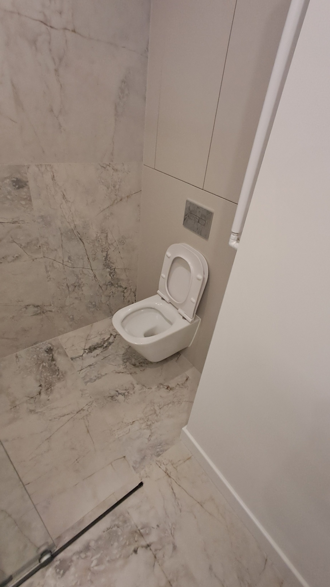 Wisząca toaleta z otwartą klapą w nowoczesnej łazience wykończonej marmurowymi płytkami.