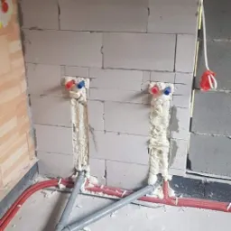 Wewnętrzna instalacja wodna w trakcie montażu w Dąbrowie Chełmińskiej: widoczne rury w ścianie z betonu komórkowego, z pianką montażową wokół przyłączy.