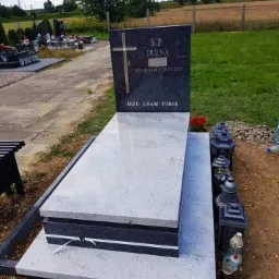 Granitowy nagrobek z wygrawerowanym krzyżem i napisem 'Jezu ufam Tobie', otoczony lampionami, zlokalizowany na cmentarzu w Żukowie.