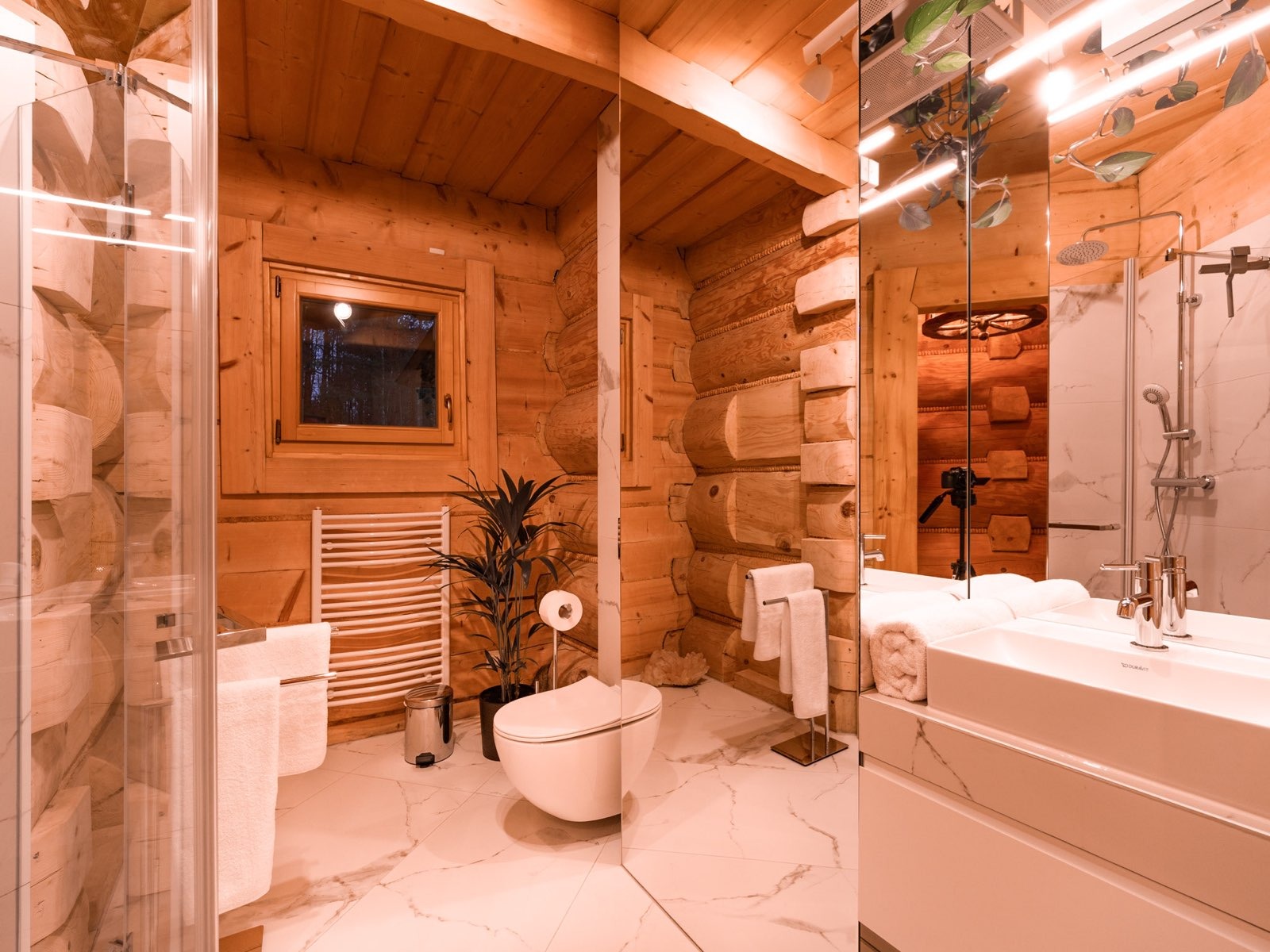 Drewniana łazienka z kabiną prysznicową, grzejnikiem drabinkowym i dużą ilością luster, w których odbijają się elementy wystroju.