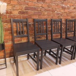 Gabinety Psychoterapii ARIADNA Katowice Raciborska - Rząd czterech ciemnych krzeseł z drewnianymi oparciami, ustawionych pod ceglaną ścianą, obok metalowego kwietnika z trawą pampasową.