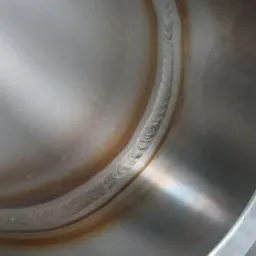 Wewnętrzna powierzchnia metalowego zbiornika z widocznym śladem spoiny, charakterystyczne przebarwienia termiczne wokół spoiny.