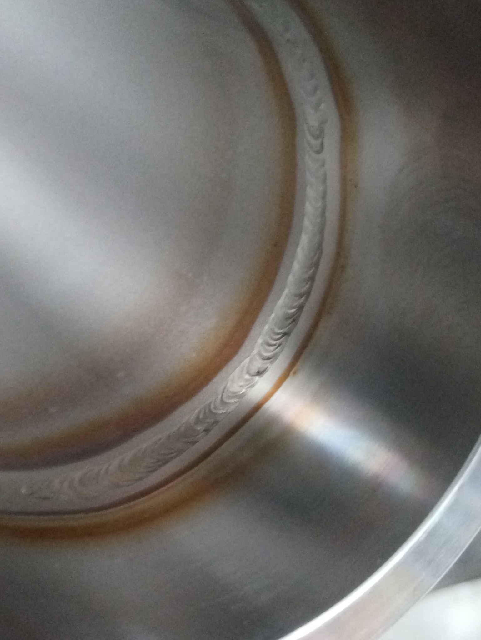 Wewnętrzna powierzchnia metalowego zbiornika z widocznym śladem spoiny, charakterystyczne przebarwienia termiczne wokół spoiny.