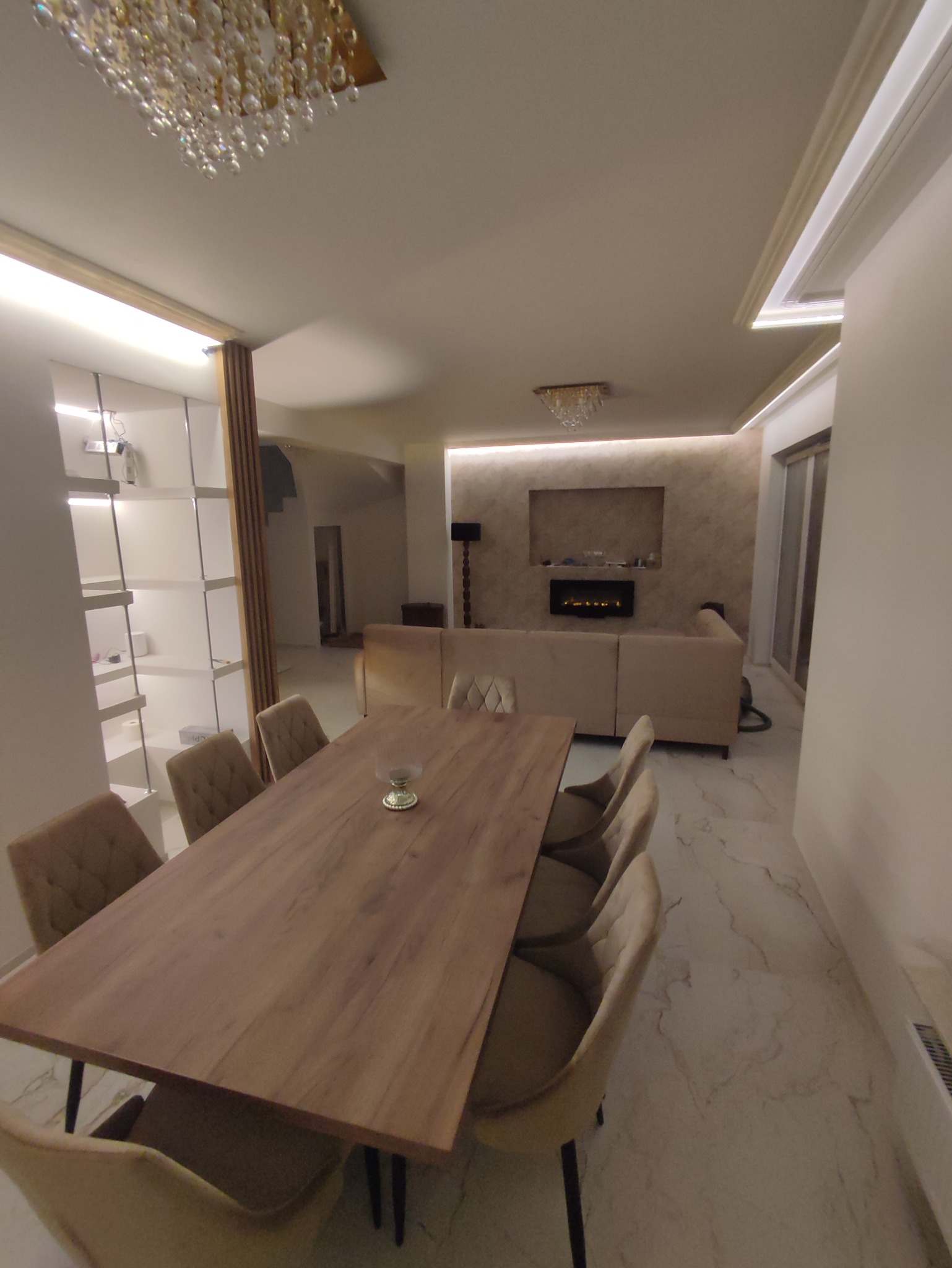 Salon z jadalnią w Warszawie po remoncie, widoczny stół z krzesłami, sofa i dekoracyjny kominek elektryczny.