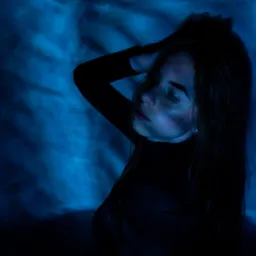 Portret kobiety w czarnym golfie na tle abstrakcyjnego, niebieskiego oświetlenia, z ręką uniesioną do włosów, delikatny kolczyk w uchu.