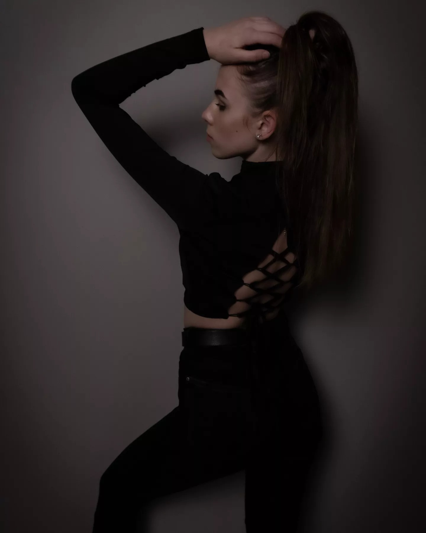 Portret profilowy młodej kobiety w czarnym ubraniu, z włosami upiętymi w wysoki kucyk, na ciemnym tle.