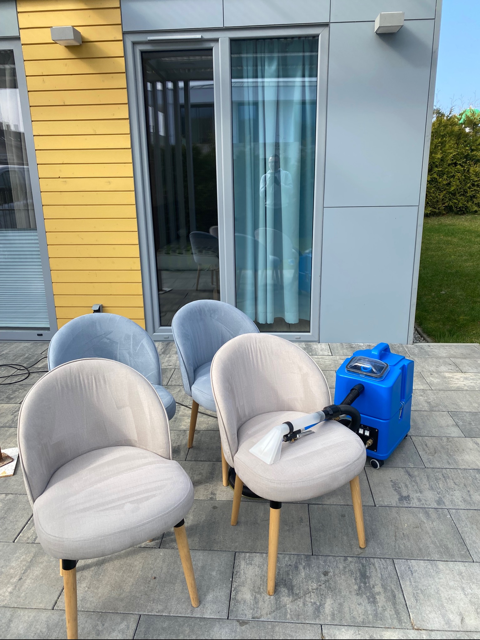Pranie krzeseł tapicerowanych na zewnątrz, z użyciem niebieskiego odkurzacza piorącego. Widoczne ślady po praniu na siedzisku krzesła.