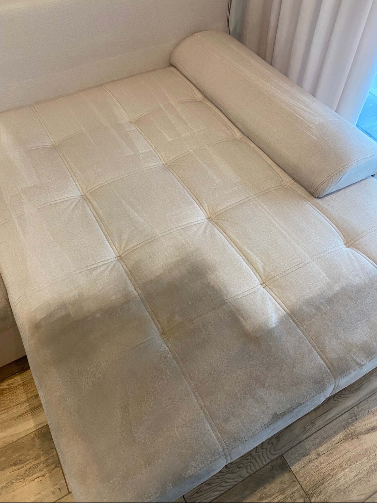 Kremowa kanapa z widoczną różnicą w czystości tapicerki po praniu, z poduszką wałkiem. Część kanapy po lewej stronie jest czystsza od prawej.