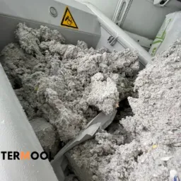 Szary materiał izolacyjny TermoWool wewnątrz maszyny do rozdrabniania, widoczny znak ostrzegawczy na górze.