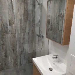 Nowoczesna łazienka z kabiną prysznicową typu walk-in z panelami imitującymi drewno, umywalką nablatową z szafką z drewna i lustrem z oświetleniem.