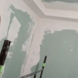 Ściany i sufit w trakcie szpachlowania, widoczne fragmenty rusztowania, na ścianach nierównomiernie nałożona gładź szpachlowa.