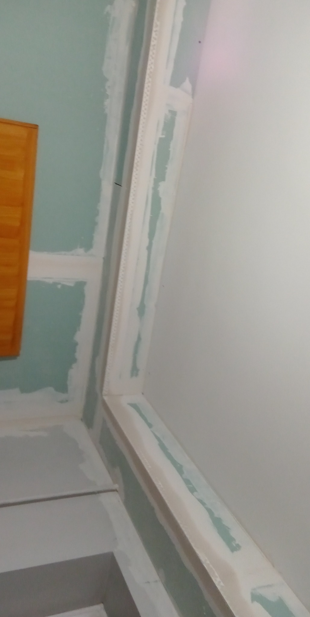 Ściana narożna z płyt gipsowo-kartonowych, w trakcie przygotowania do wykończenia, widoczne łączenia płyt pokryte masą szpachlową, listwa narożna zamontowana.