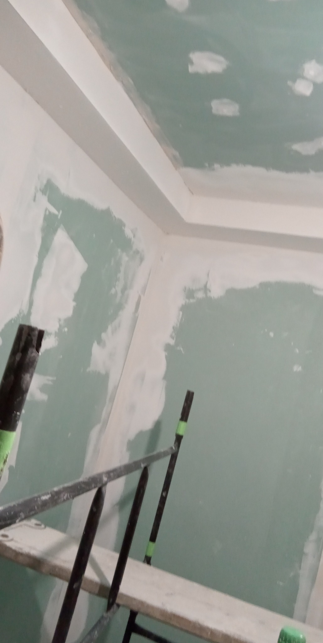 Ściany i sufit w trakcie szpachlowania, widoczne fragmenty rusztowania, na ścianach nierównomiernie nałożona gładź szpachlowa.