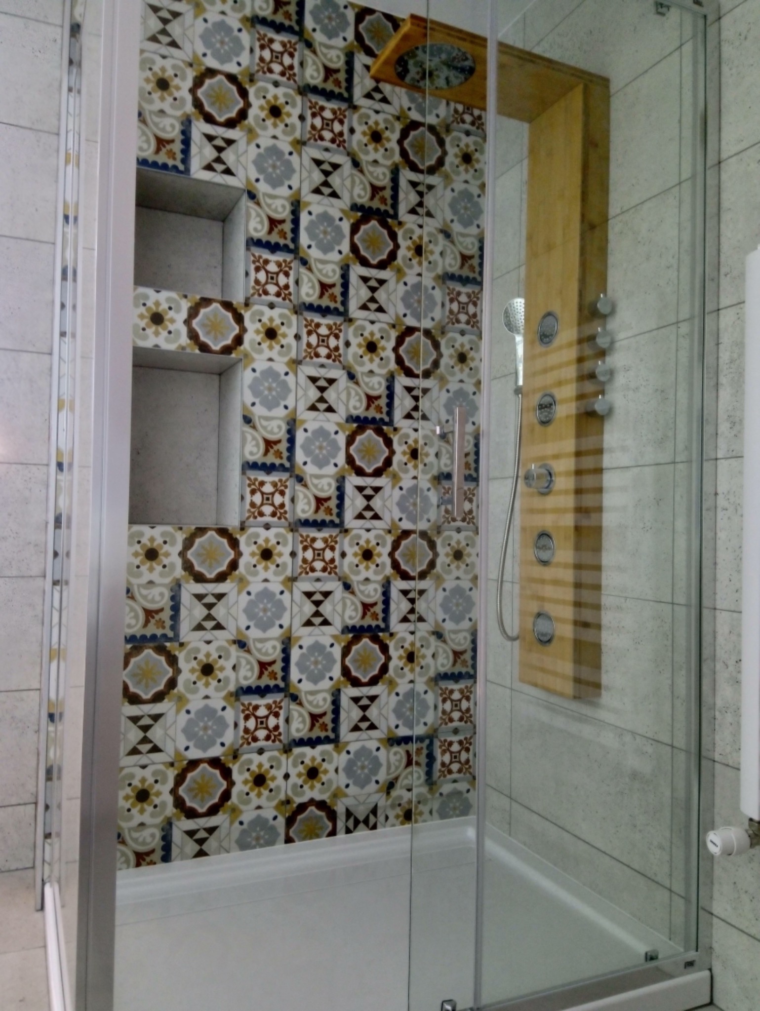 Kabina prysznicowa z deszczownicą i panelem hydromasażu, wyłożona wzorzystymi płytkami ceramicznymi z wnękami na kosmetyki.