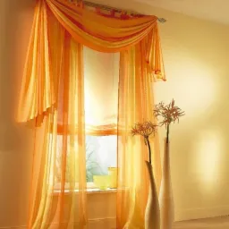 Aranżacja okienna z pomarańczowych, zwiewnych firan i rolet rzymskich, dopełniona wysokimi, smukłymi wazonami z dekoracyjnymi gałązkami.