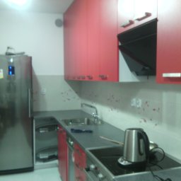 Alfa Producent mebli - Czerwono-szara kuchnia z blatem w kolorze grafitu, wyposażona w srebrną lodówkę i czajnik elektryczny na płycie grzewczej.