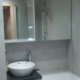 Alfa Producent mebli - Nowoczesna łazienka z umywalką nablatową na szafce z szarym blatem, duże lustro z odbiciem kabiny prysznicowej, obok wanna.